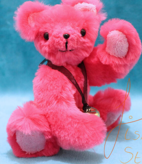 a little pink jointed teddy bear waving hello. it has a bell around it's neck. Made of faux fur and minky fabrics