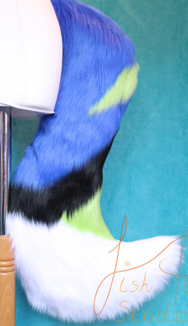 Large Fursuit Wolf Tail commissioned out of luxury faux fur. it is blue with green, black and white accents. designed on our base wolf tail pattern, it connects to a belt using belt loops. made by fishpish studios