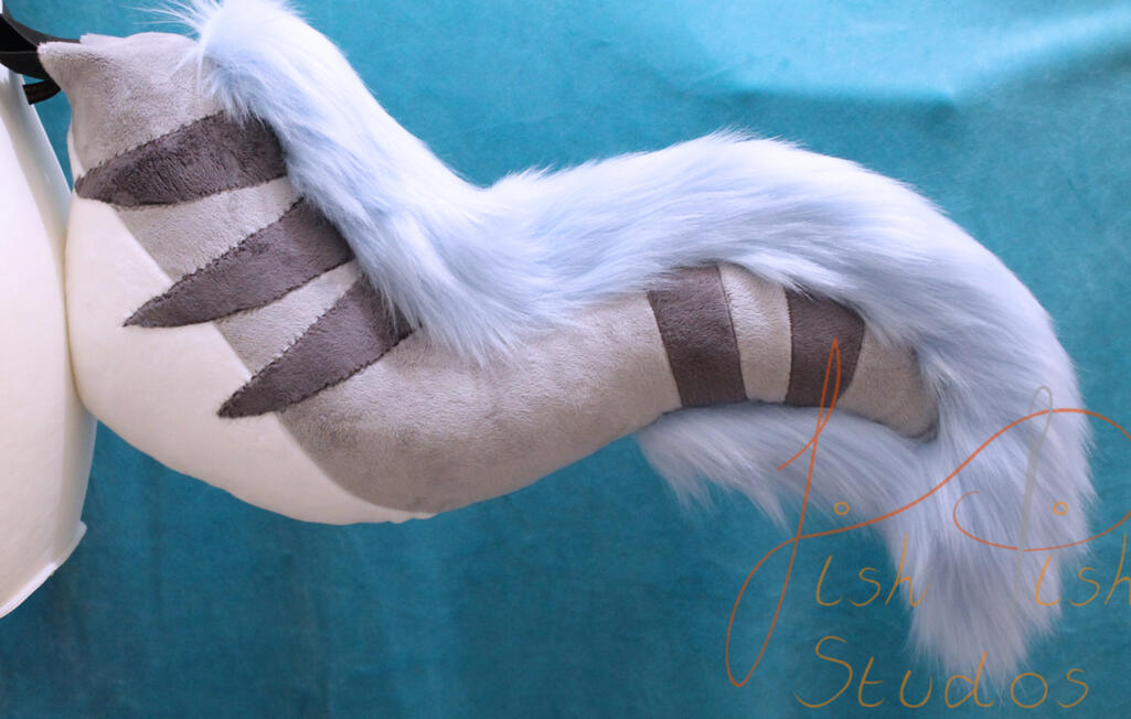 Striped XYX Fursuit Tail a competition prize won on bluesky. it's made of various grey and cream minky/soft plush fabrics and a baby blue luxury faux fur. it sticks out about 21 inches, and is soft to the touch. designed by the winner and made by fishpish studios