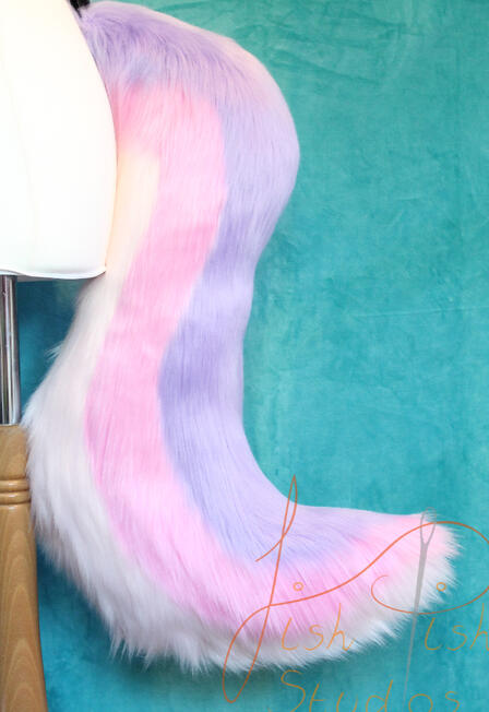 Pink and Lilac 3 Stripe Wolf Tail A long, 25 inch, luxury faux fur wold tail with stripes running from the base to tip in an 's' type curve. Top colour is lilac, then a pale pink with the underside as white. There are belt loops to hold the tail to a belt, this is designed and made by fish