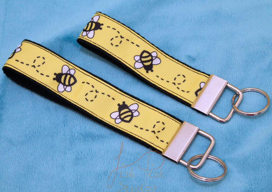 Bee Key Fob Keyring a cute photo showing two bee themed keyrings made of fabric. one is slightly bigger than the other. Both have little cartoon bees on them with a yellow background. handmade in the UK by fishpish studios
