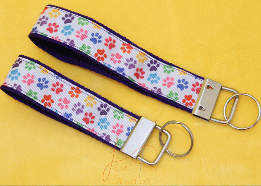 Colourful Paw Prints Key fob keyring a cute photo showing two colourful paw print themed keyrings made of fabric. one is slightly bigger than the other. Both have little cartoon paw prints on them with a white background. handmade in the UK by fishpish studios