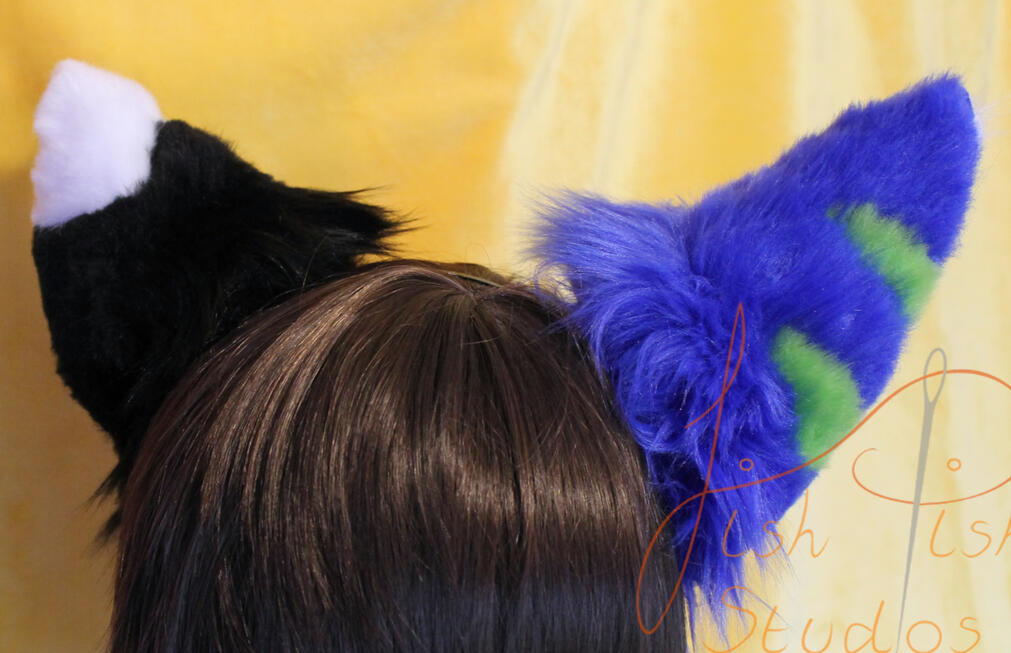 Commissioned Asymmetrical Furry ears A pair of complex asymmetrical wolf ears commissioned by a client. One is black with a white tip, the other blue with green stripes. Made of luxury faux fur, these are posable on a metal headband. Handmade by fishpish studios in the UK